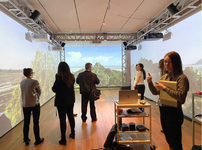 a group of people standing in front of a room full of screens showing a beautiful landscape